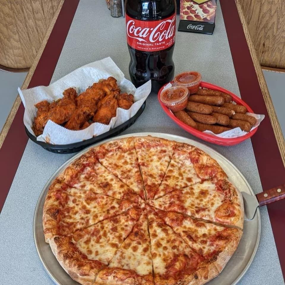 A pizza , coca cola , chicken wings and sausages are on a table.