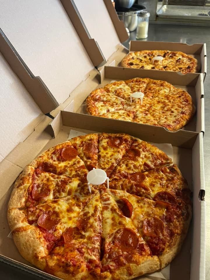 Three pizzas are sitting in cardboard boxes on a table