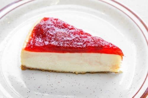 A slice of strawberry cheesecake on a white plate.