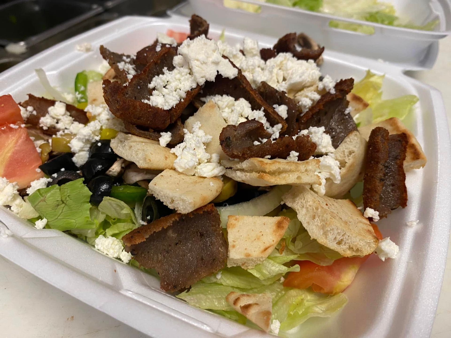A gyro salad in a styrofoam container on a table.