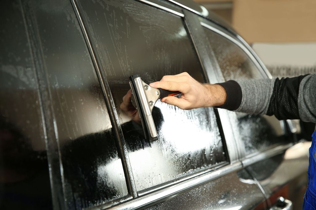 Worker spray-painting a car fender in a body shop, wearing a respirator and gloves
