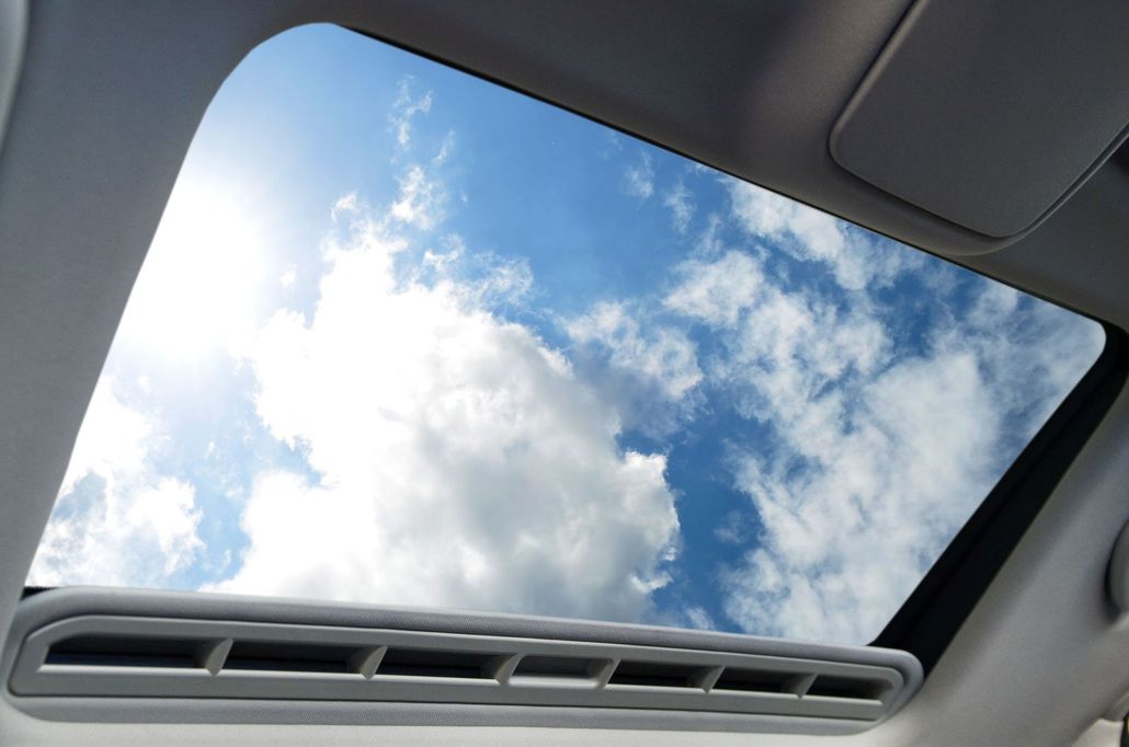 Car sunroof view of blue sky with white clouds and roof controls at the bottom