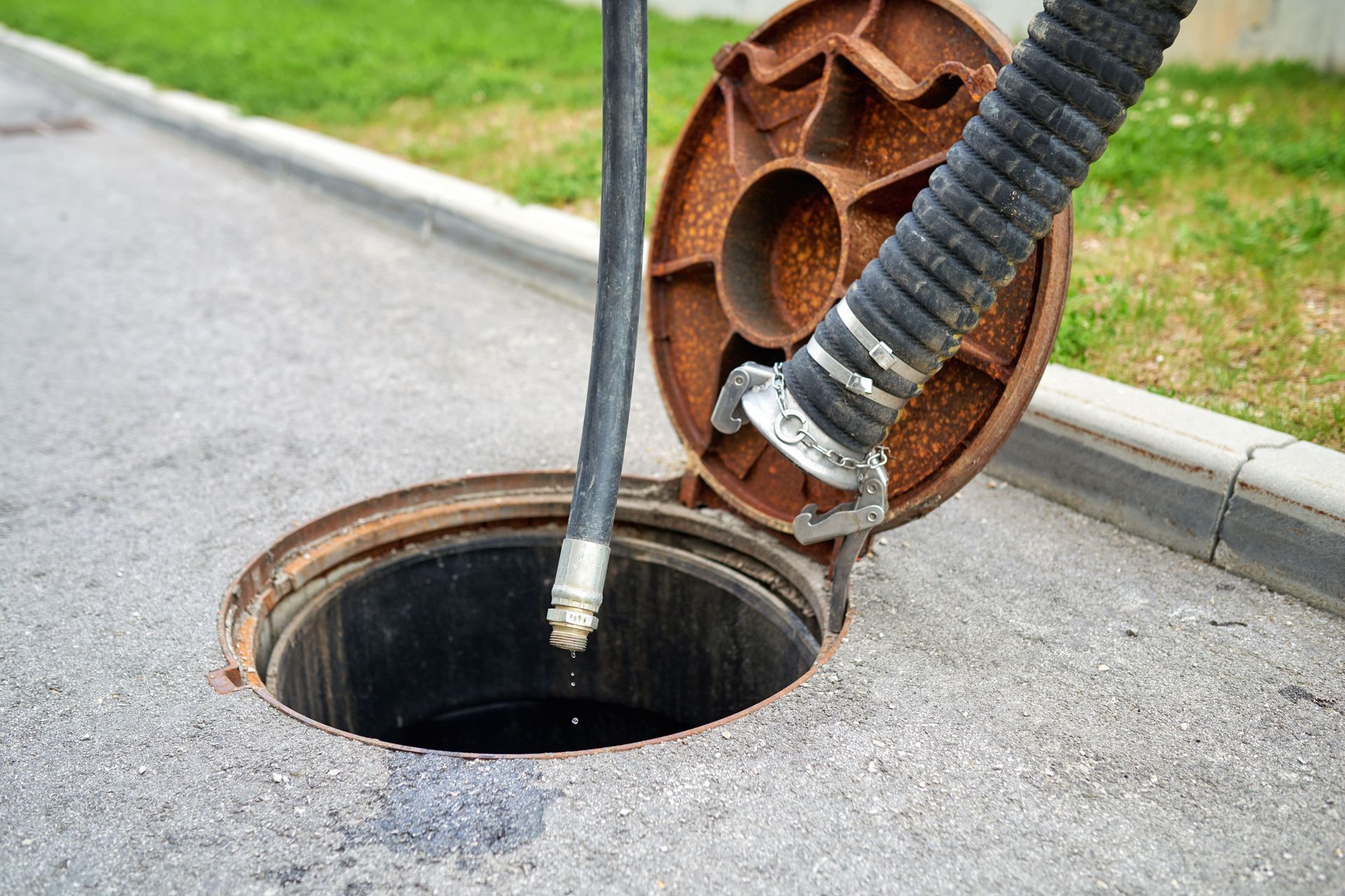 Suction hose cleaning a round manhole opening beside a curb on a street