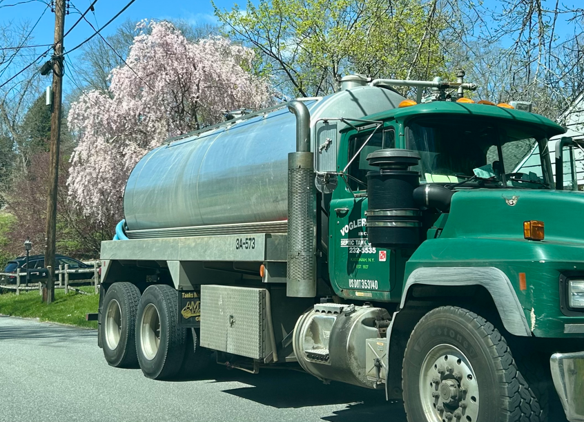 Green water tanker truck parked on a tree-lined street in spring