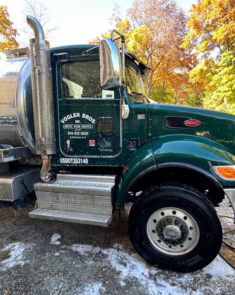 Dark green semi truck parked outdoors in autumn, with chrome exhaust and steps, on snowy ground.