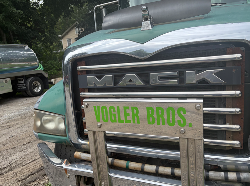 Close-up of a teal Mack truck grille with a Vogler Bros. sign on the front.