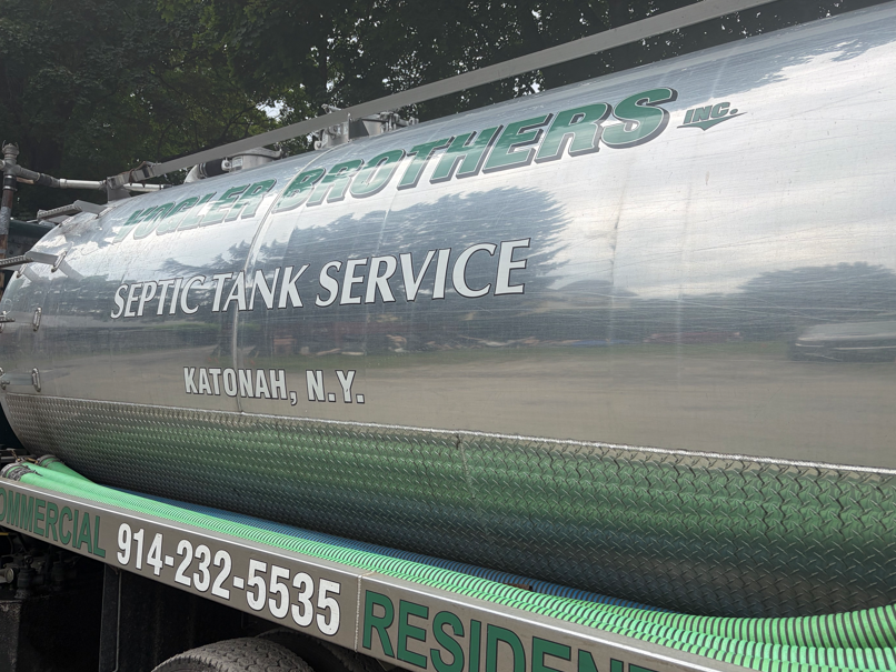 Silver septic tank service tanker truck with green lettering and phone number 914-232-5535