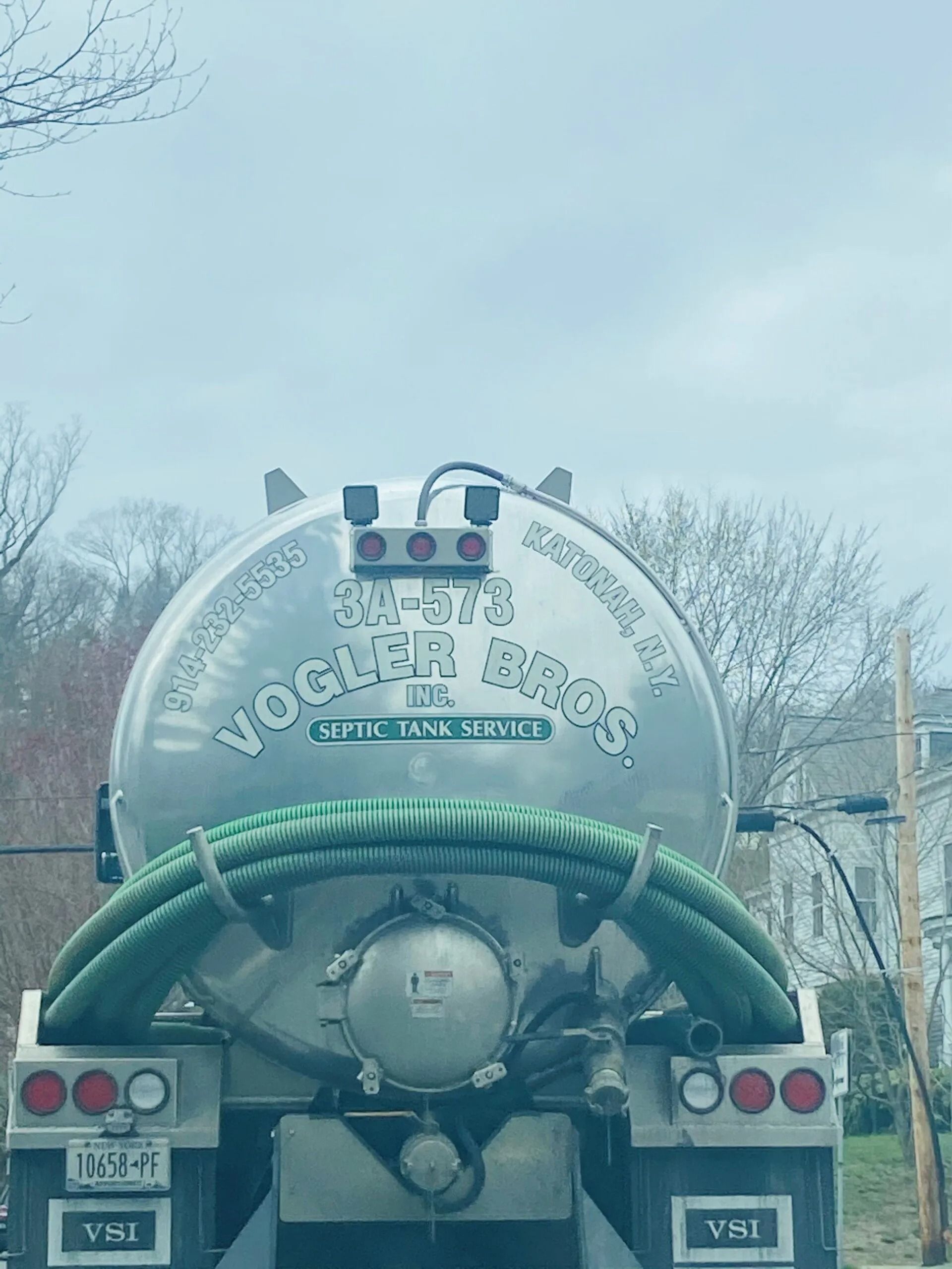 Rear view of a silver truck with a green hose and Cyrillic lettering on the back, parked outdoors under a cloudy sky