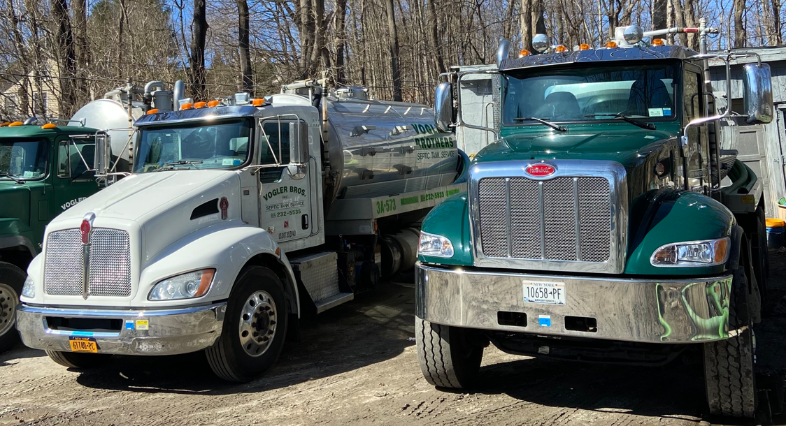 Two parked semi trucks, one white and one green, in a snowy outdoor lot