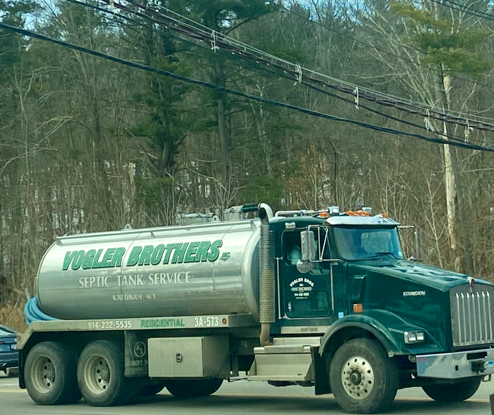 Green tanker truck labeled “Taylor & Bowers” parked on a roadside with trees in the background
