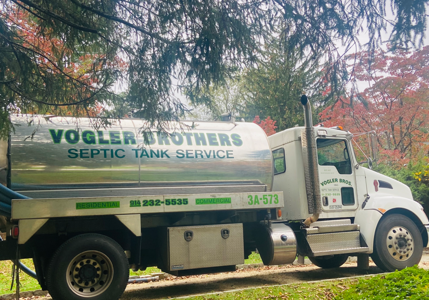 White septic tank service truck parked under trees with “Vogler Brothers” lettering on the side.