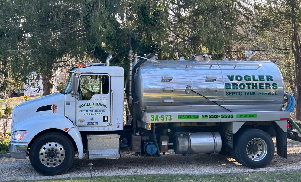White water tanker truck labeled “Vogler Brothers” parked outdoors by trees.