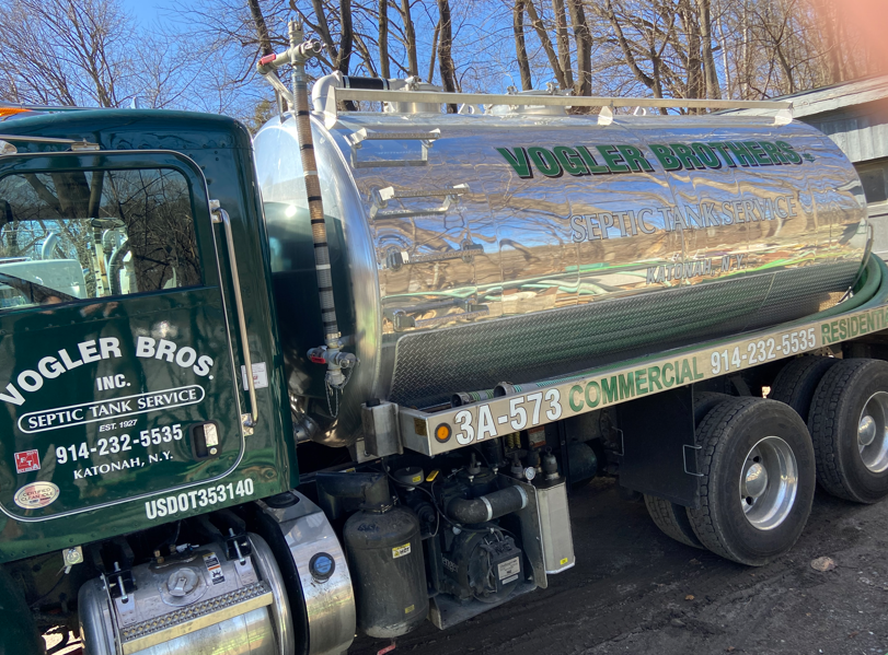Chrome Vogler Bros commercial waste truck parked outdoors with trees reflected on its tank.