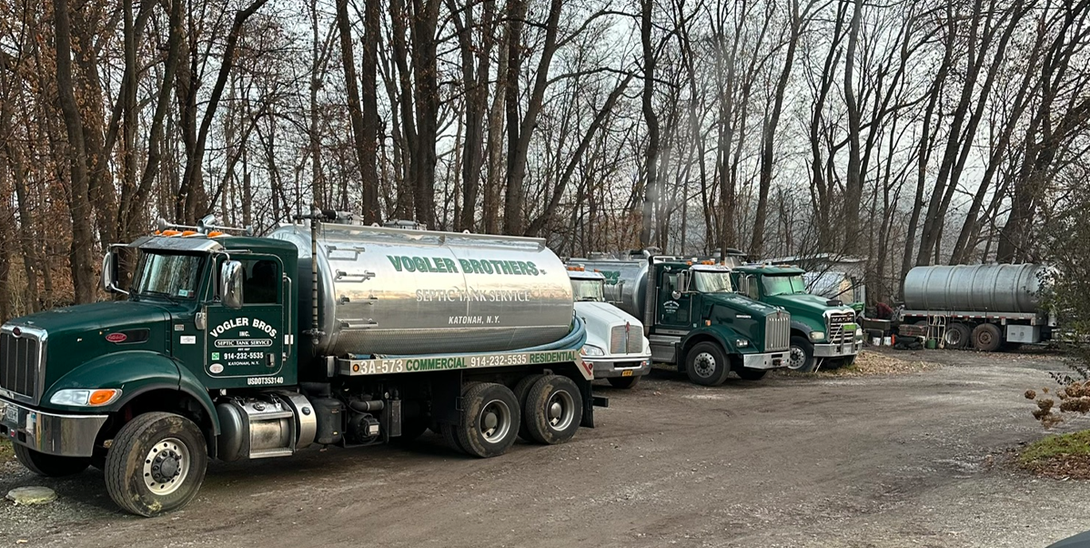 Three green tanker trucks parked in a wooded clearing beside a dirt road