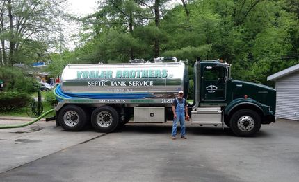 Large green tanker truck parked on a driveway, with a person standing beside it and trees in the background.