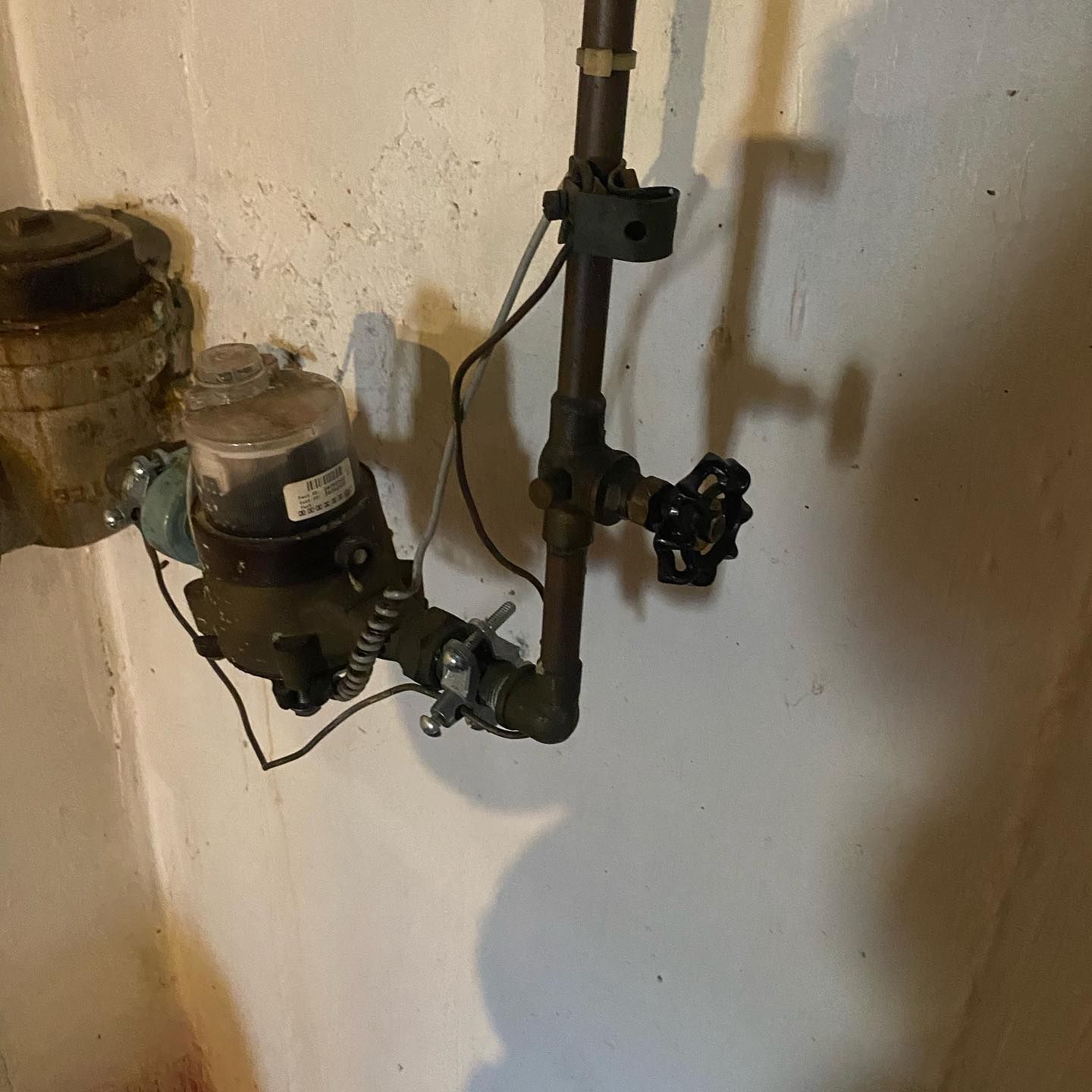 Water meter and valve attached to copper pipes against a white wall.