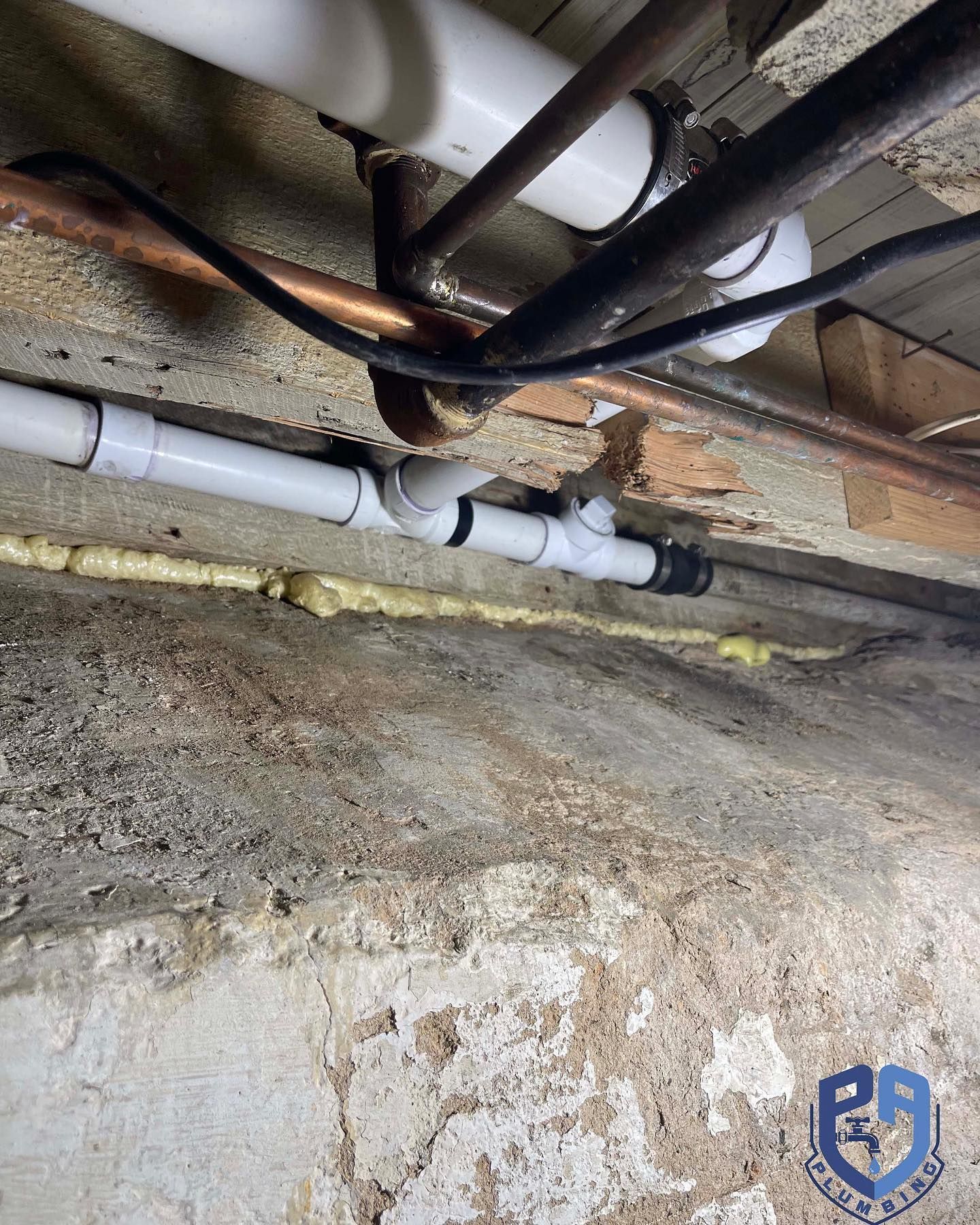 Pipes in a basement; white PVC and copper pipes against a concrete wall, yellow foam sealant.