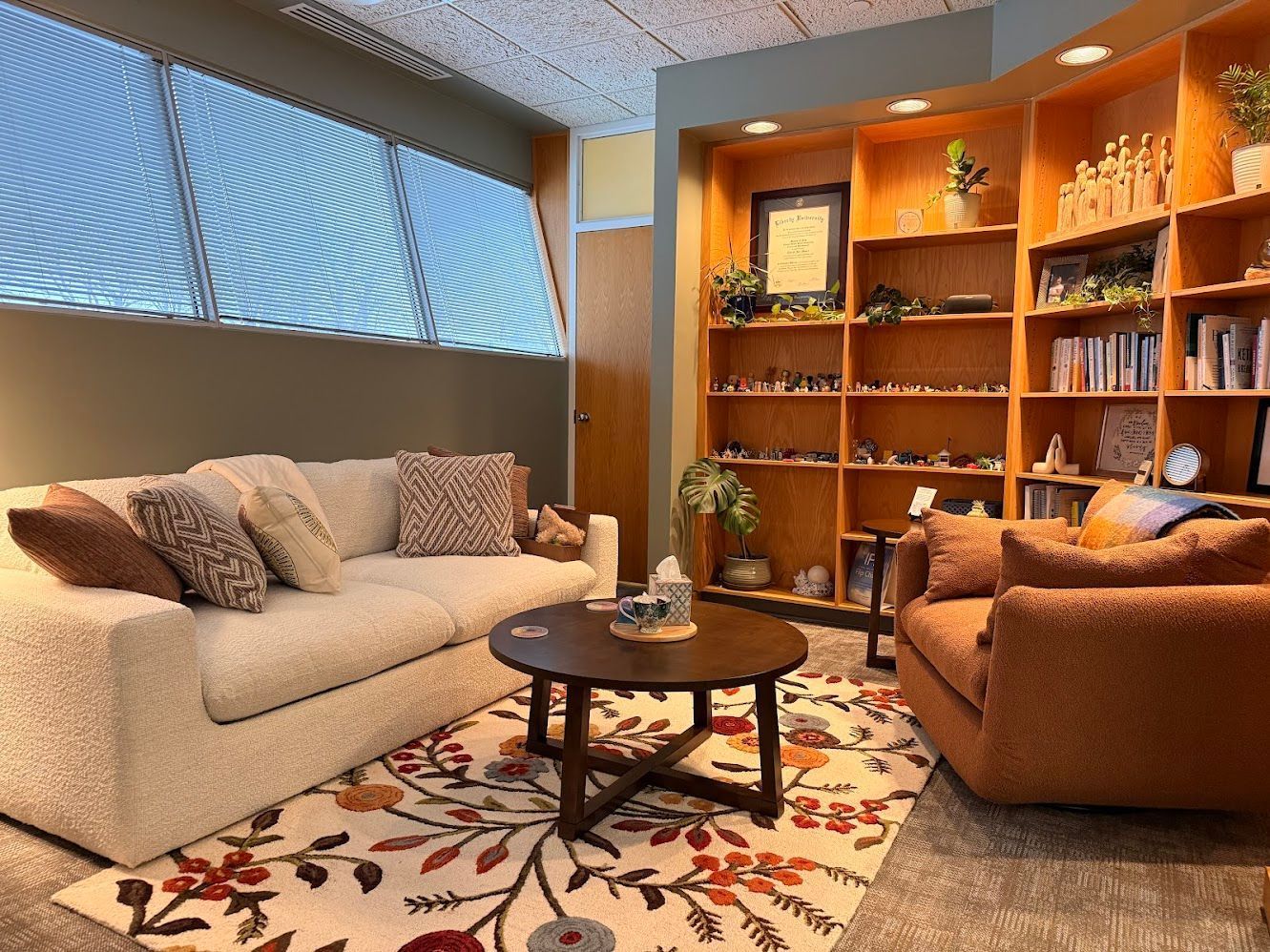 Cozy living room with beige sofa, brown chair, round table, floral rug, and wooden shelves.