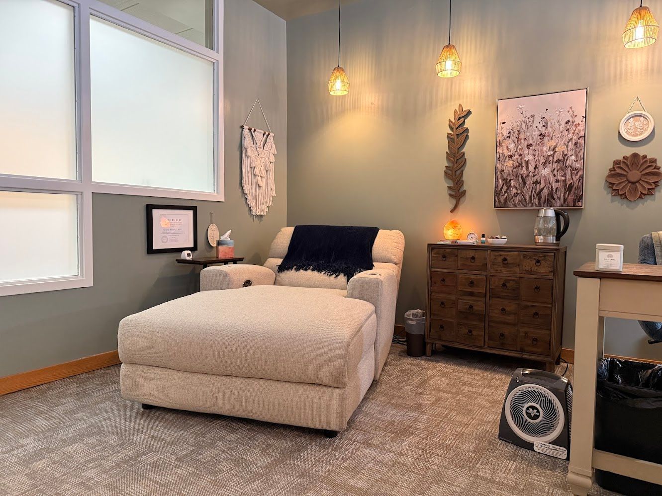 Cozy spa room with massage table, warm pendant lights, dresser, and soft beige decor.