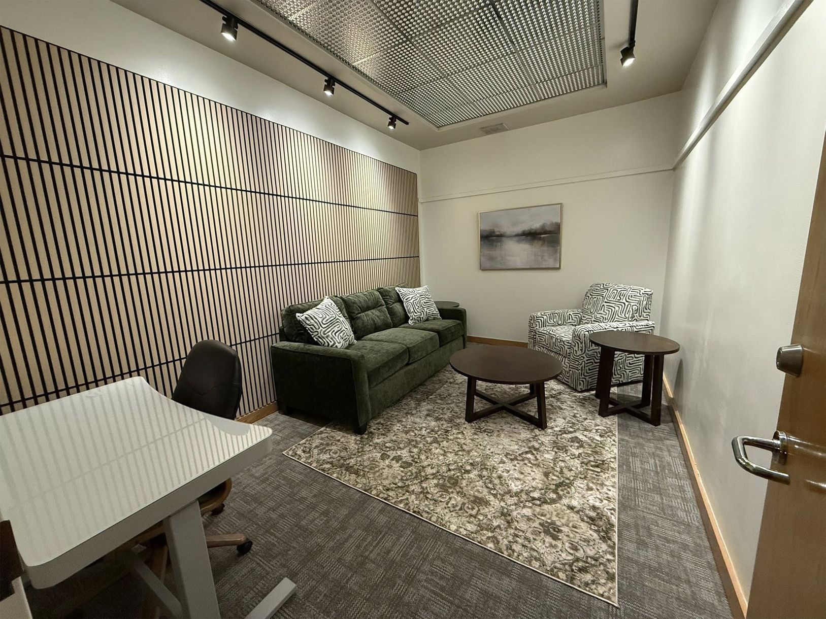 A small, modern office space with a couch, armchair, table, and decorative wall paneling.