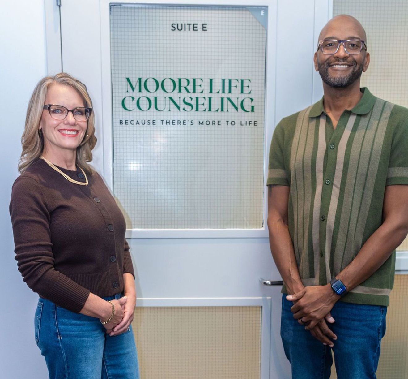 Two people in front of a door. Woman in brown and man in green, by Moore Life Counseling sign.
