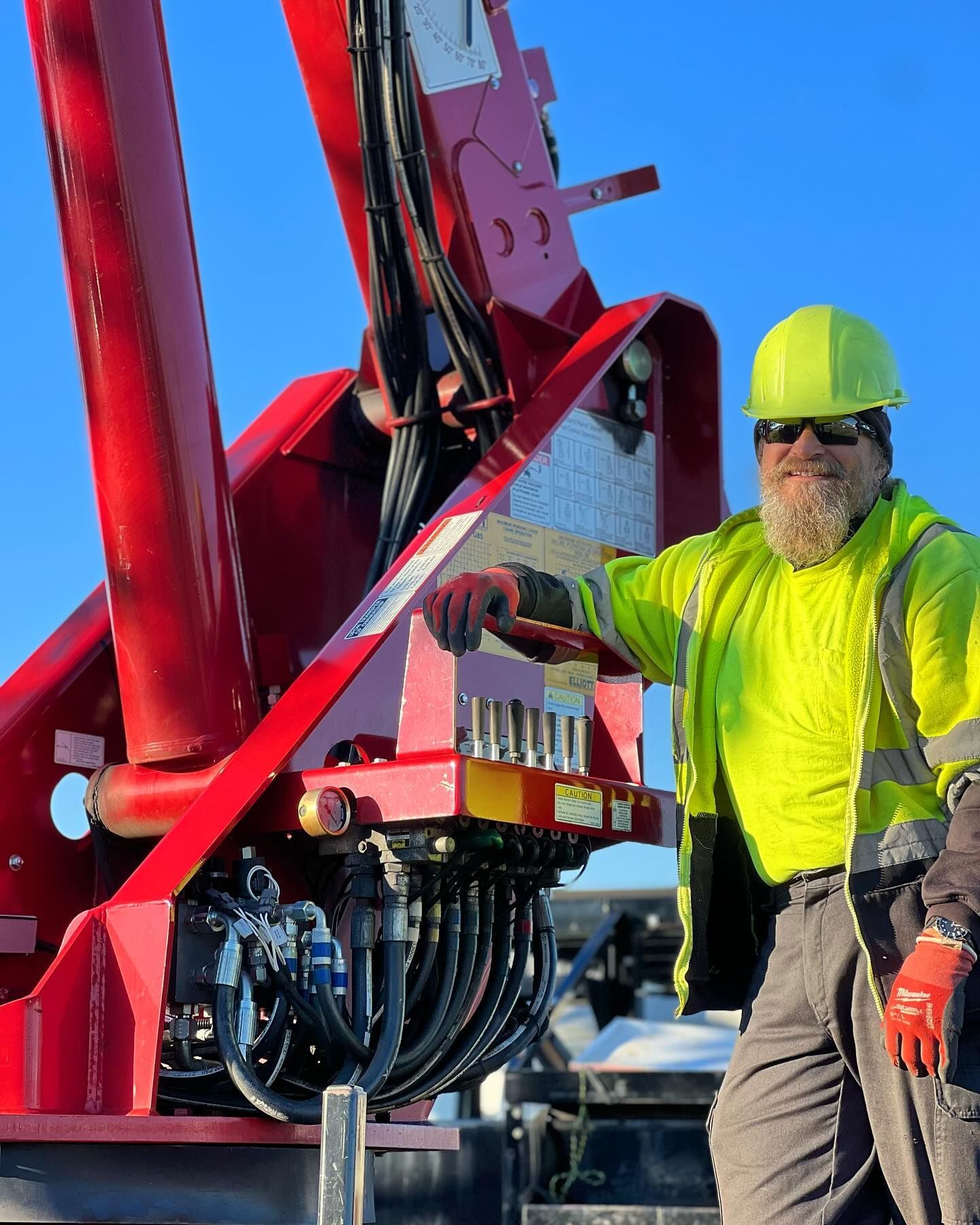 A man in a yellow hard hat is standing next to a red crane.