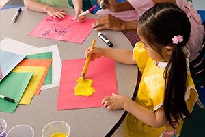 A little girl is sitting at a table painting with a brush.