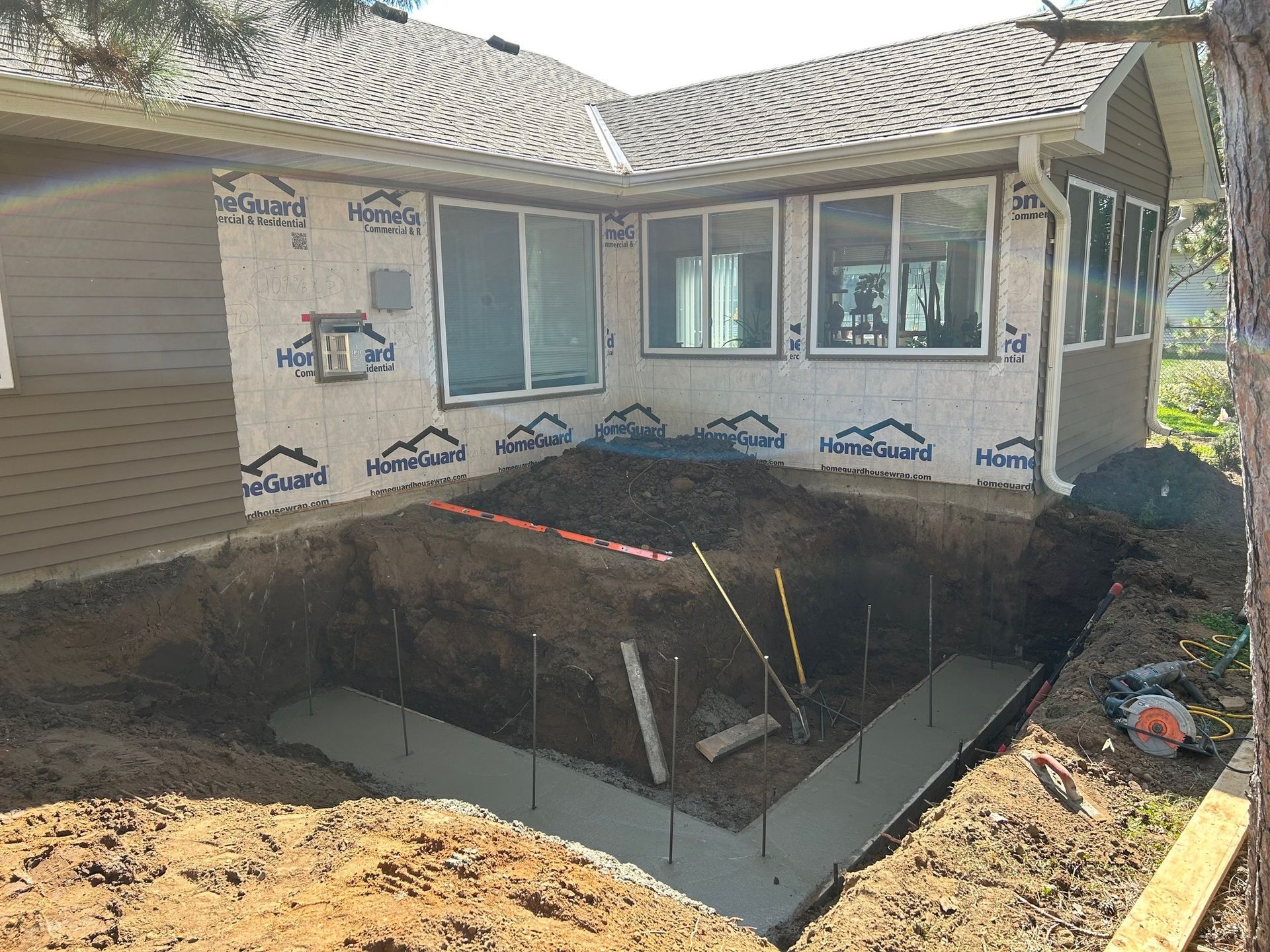 A house is being built with a large hole in the ground in front of it.