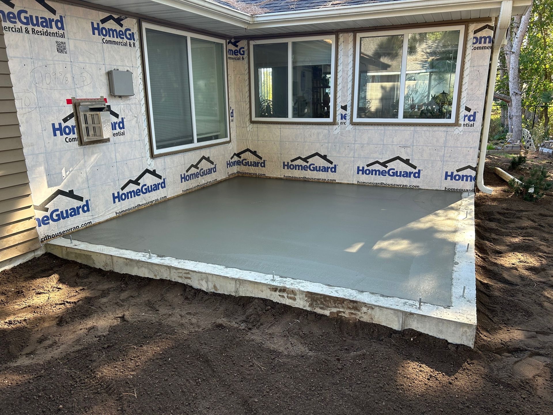 A concrete patio is being built in the backyard of a house.