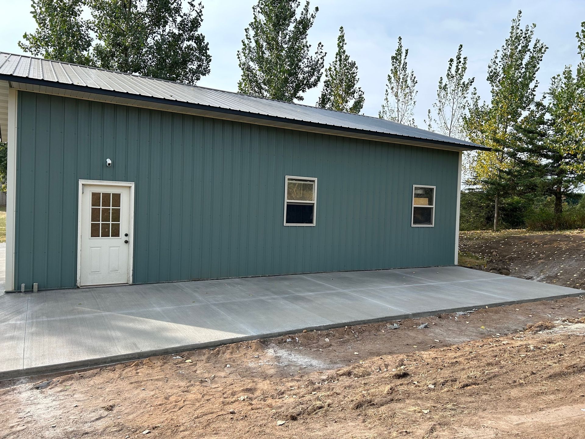 A green metal building with a concrete driveway in front of it.