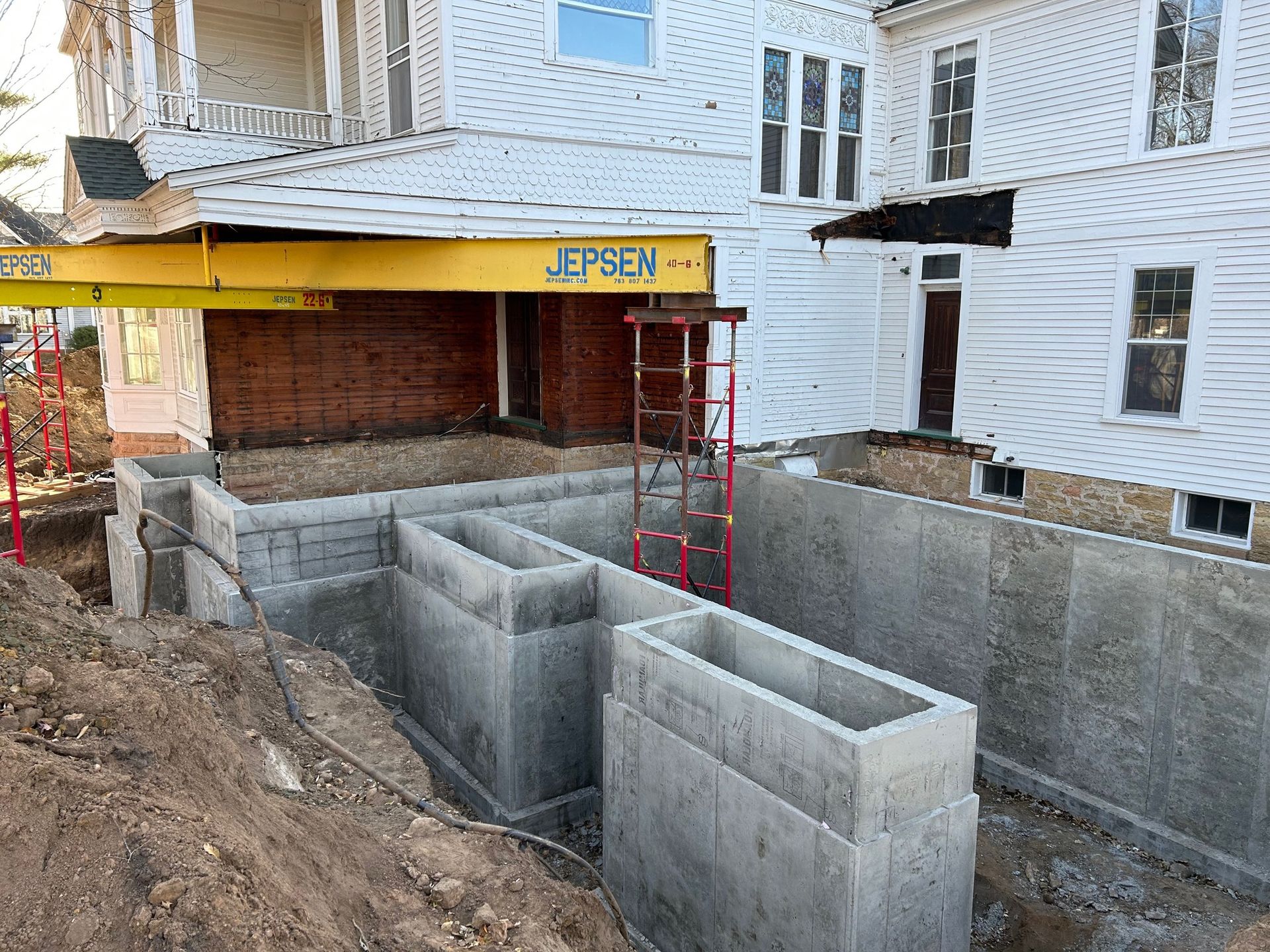A yellow crane is being used to lift a concrete wall in front of a house.
