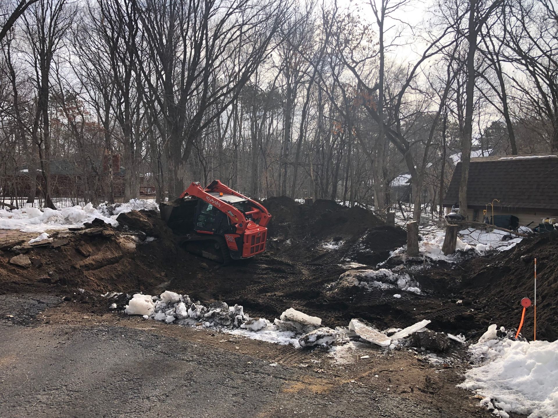 A bulldozer is digging a hole in the snow in the woods.