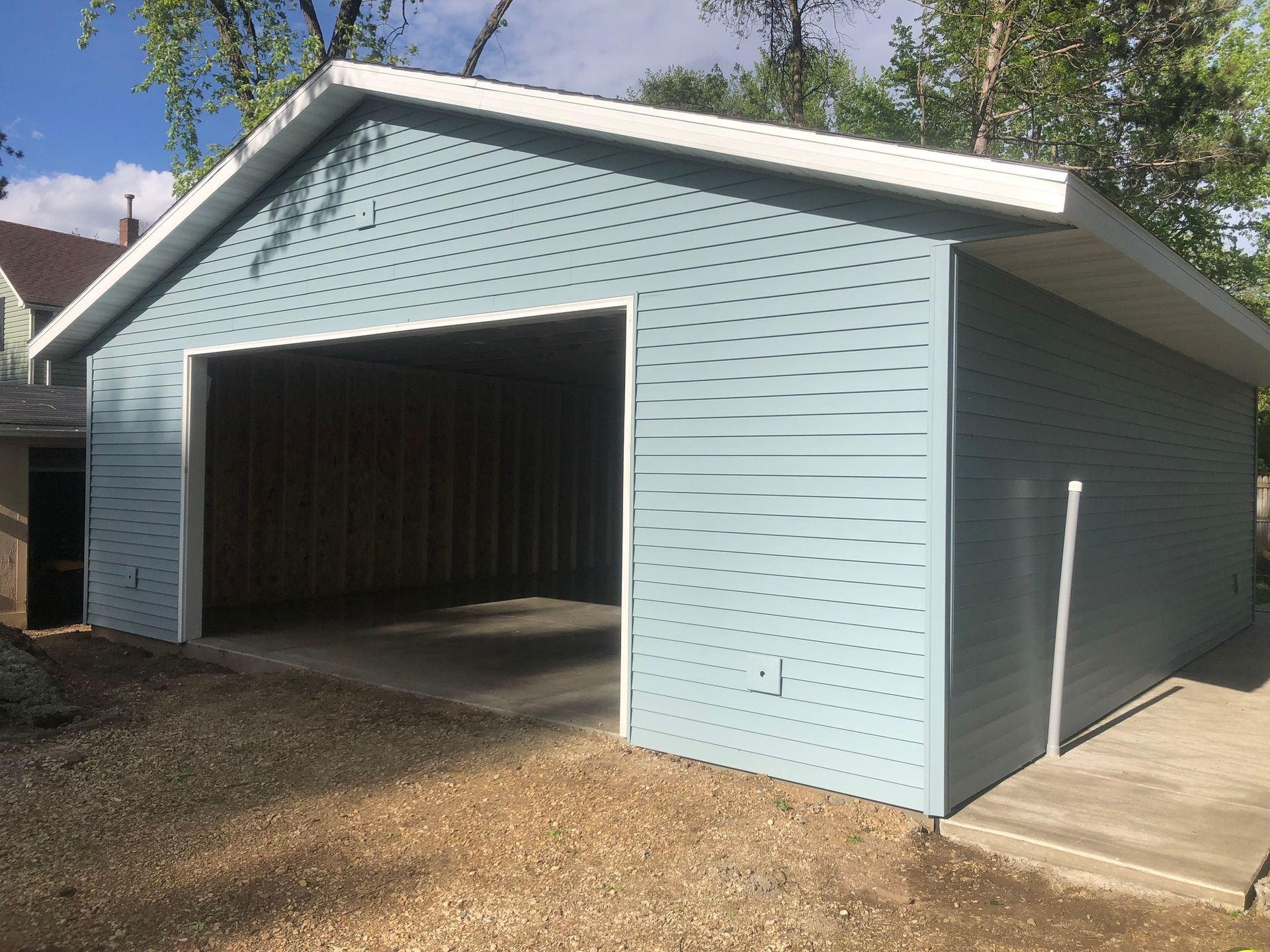 A blue garage with a white roof is sitting on top of a gravel lot.