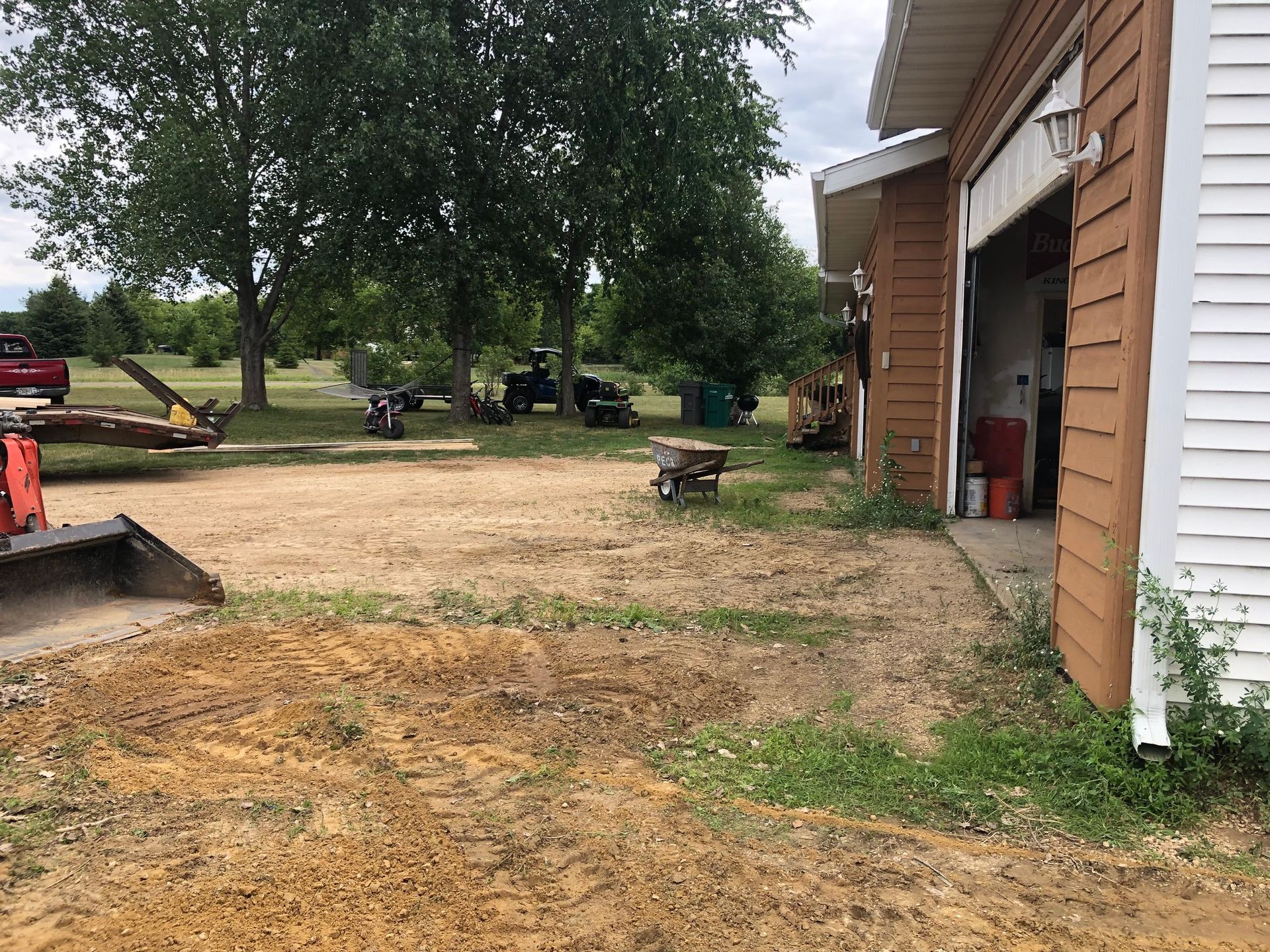 A tractor is parked in the dirt in front of a garage.