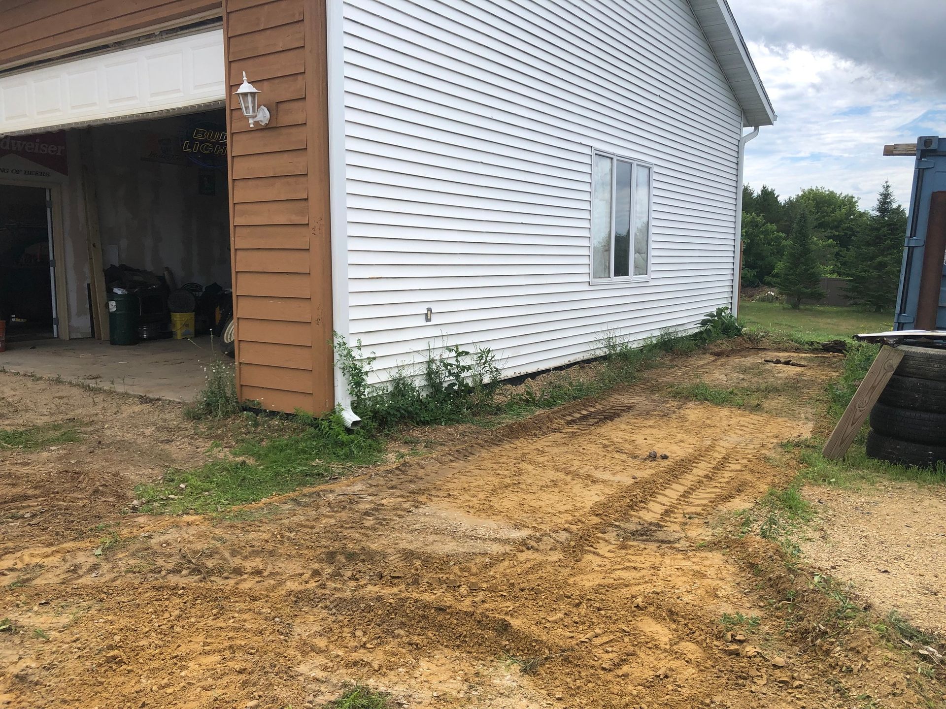 A white house with a garage door is sitting next to a dirt road.