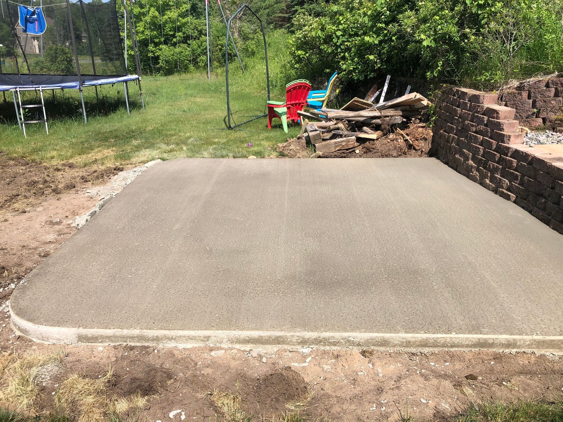 A trampoline is sitting on top of a concrete platform in a backyard.