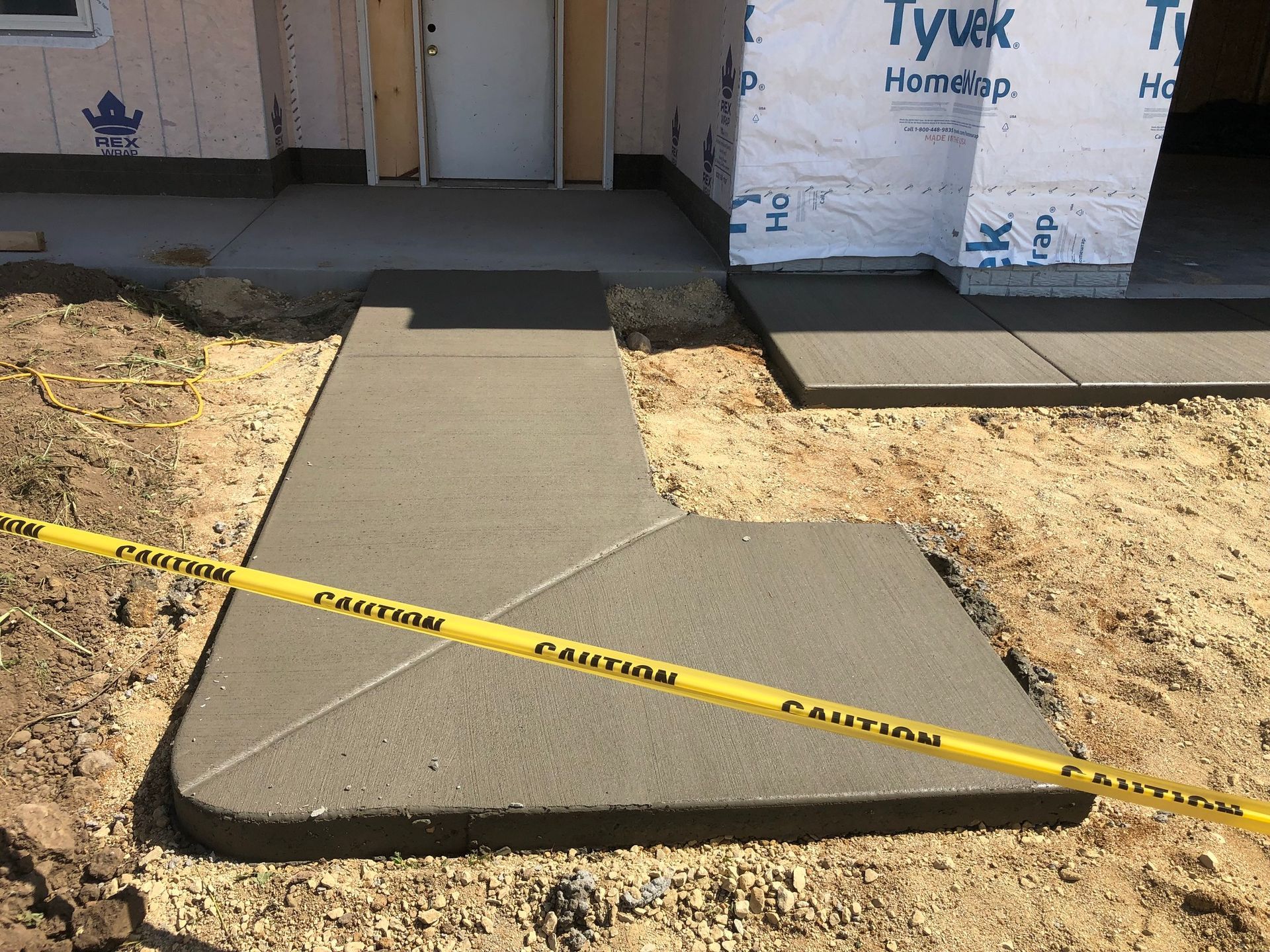 A concrete walkway is being built in front of a tyvek building