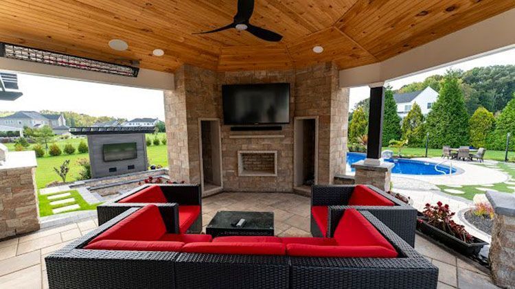A patio with a couch , chairs , a fireplace and a flat screen tv.
