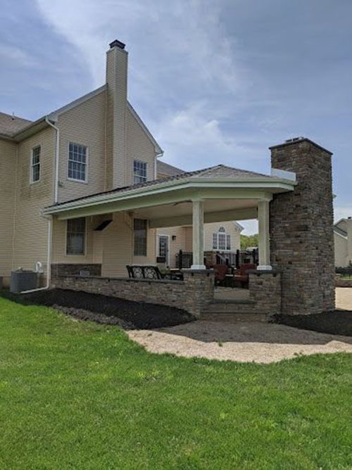 A large house with a porch and a fireplace in the backyard.