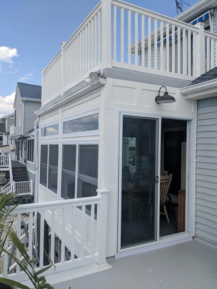 White beach house with balcony and deck, sliding glass door, outdoor lighting and deck.