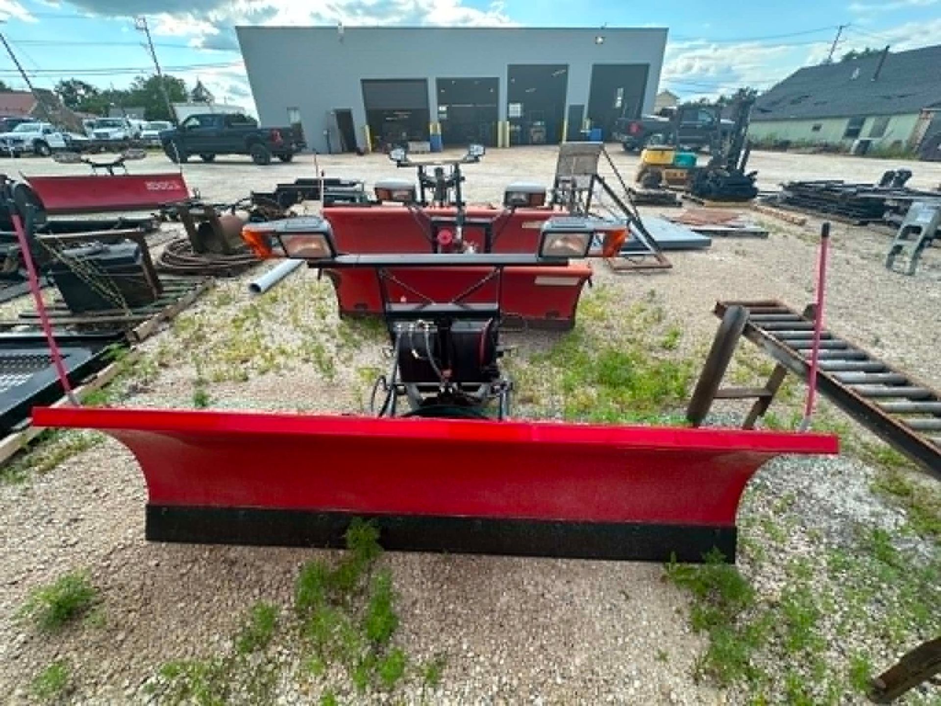 Red snow plow blades and heavy equipment lined up in an industrial yard.