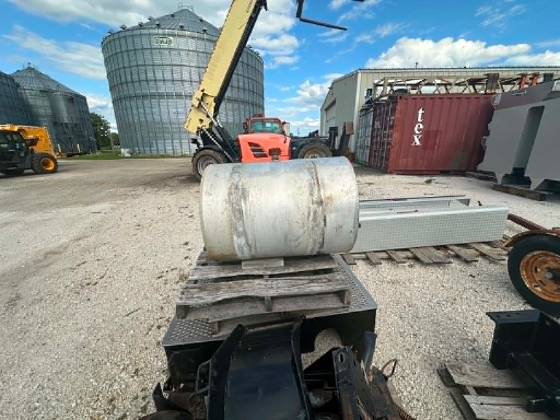 Construction site with a large metal cylinder on a platform, heavy machinery, and storage containers under a blue sky