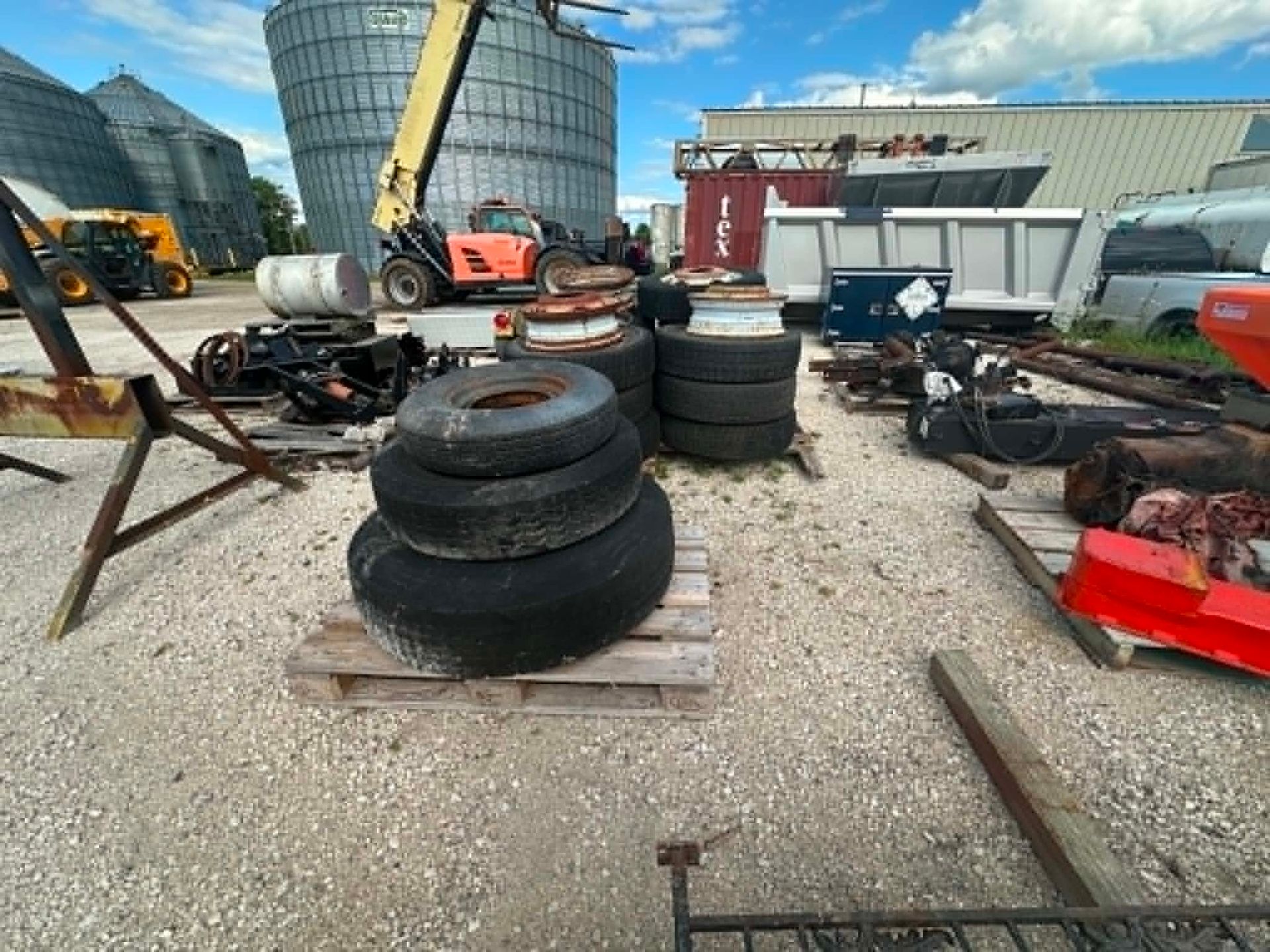 Outdoor scrapyard with stacked tires, scattered metal parts, and red machinery under a blue sky