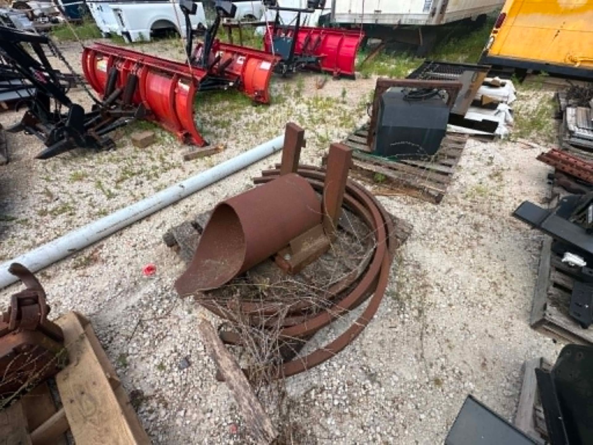 Rusty metal farm equipment and scrap parts scattered on gravel in an outdoor yard.
