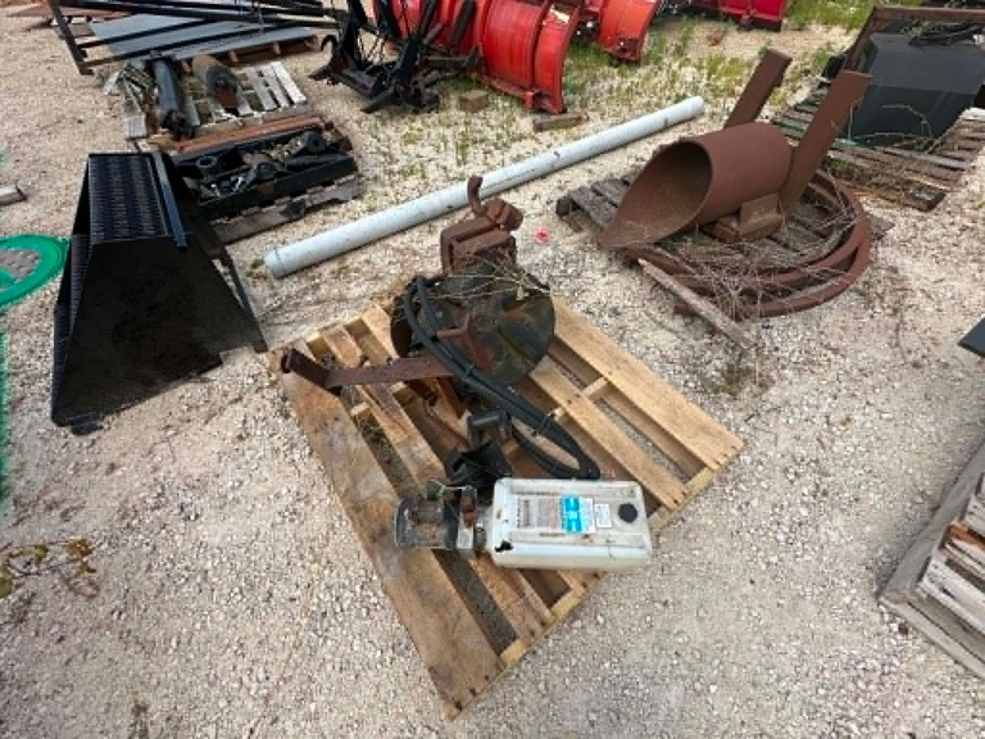 Rusty machinery parts and a chain block on wooden pallets in a gravel yard.