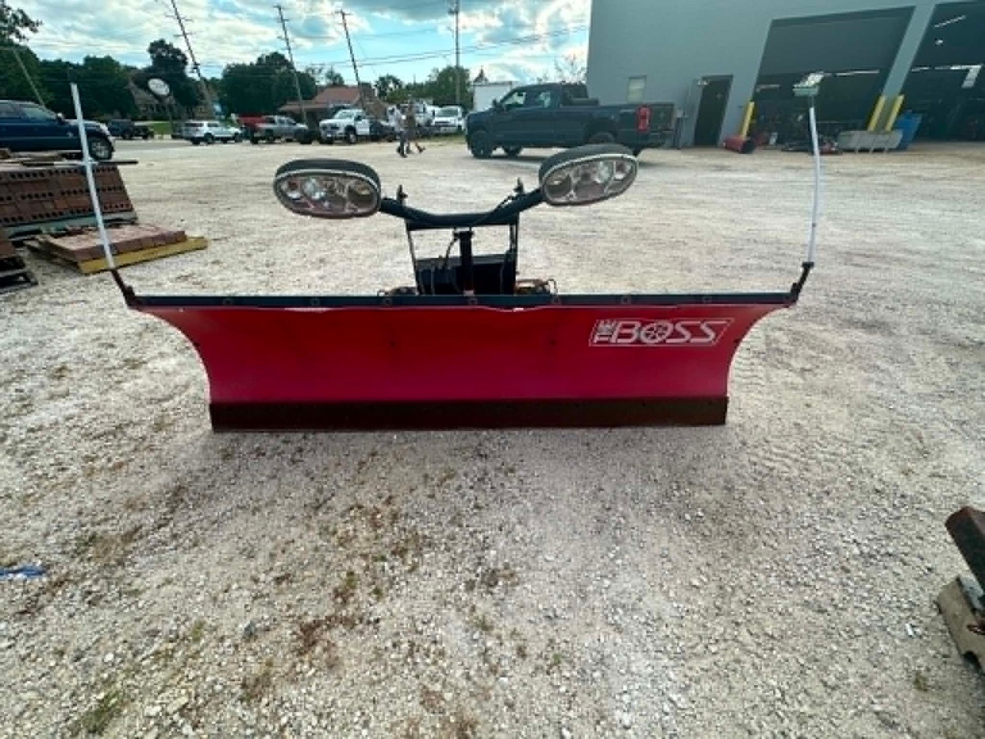 Red Boss snow plow blade with dual side mirrors on a gravel lot