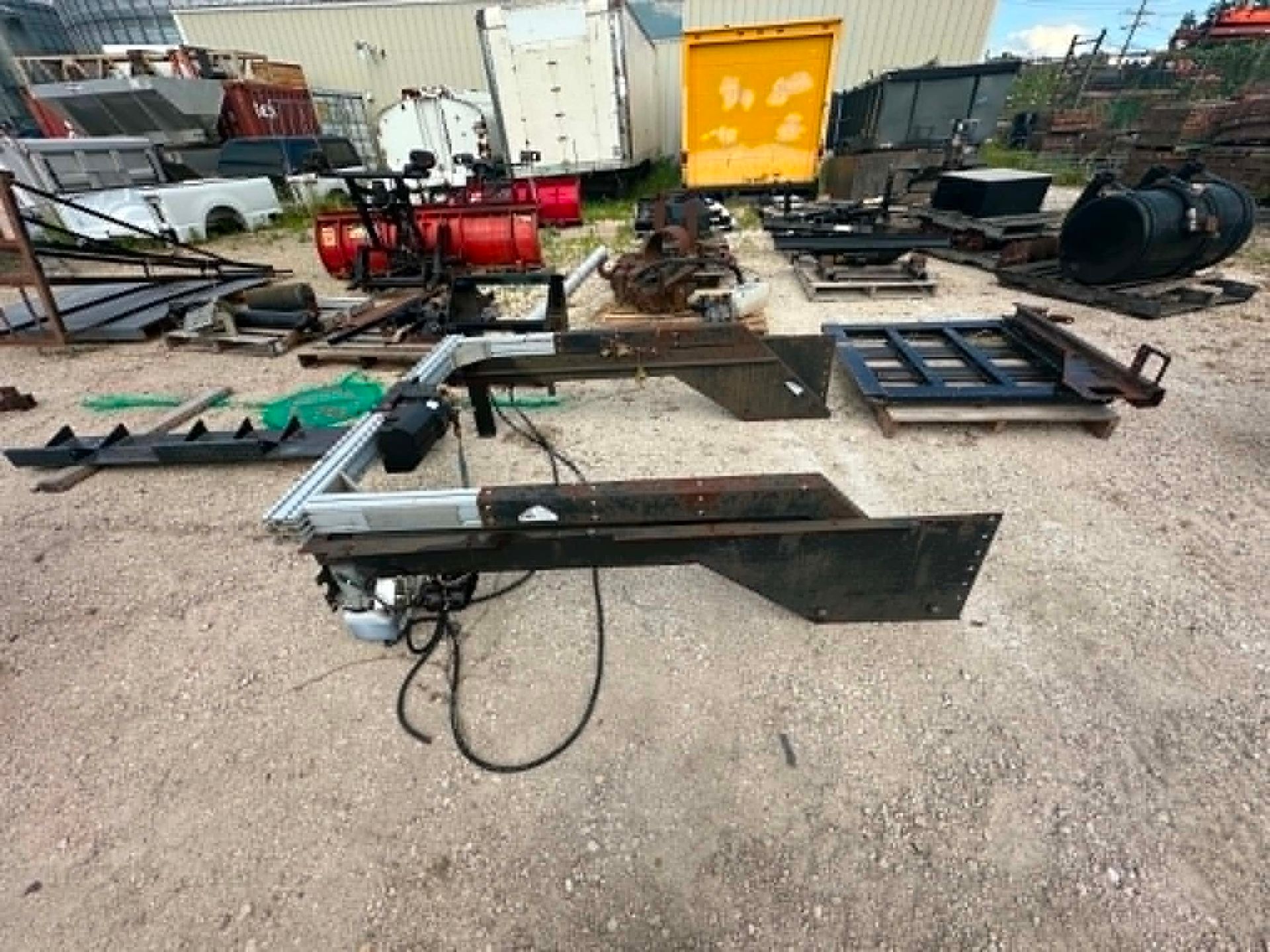 Industrial yard with assorted metal equipment, pipes, and machinery parts on gravel.