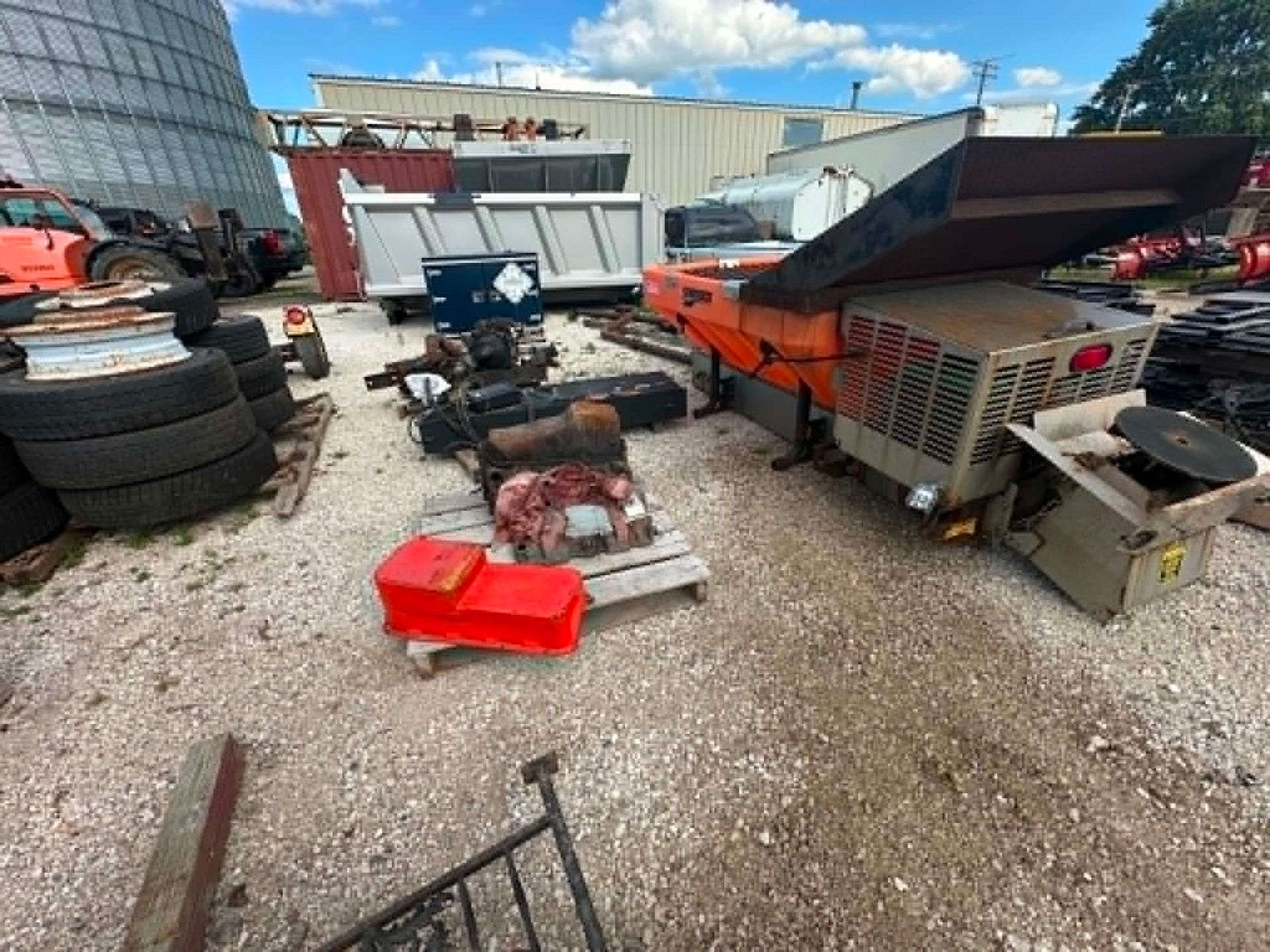 Outdoor auto repair yard with tires, tools, and a red industrial machine on gravel.