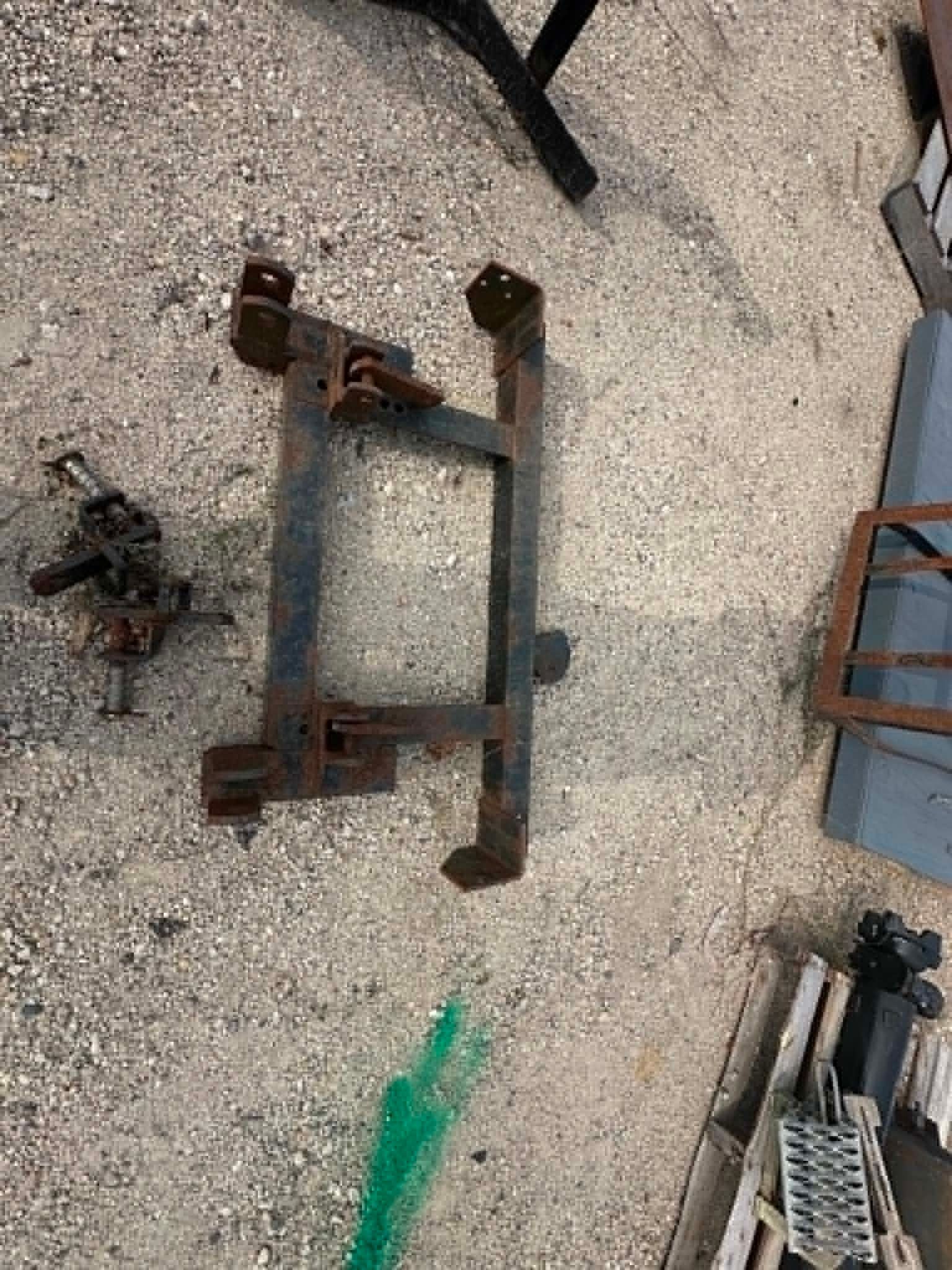 Rusty metal machinery parts laid on gravel, with a green strap and a blue structure nearby.