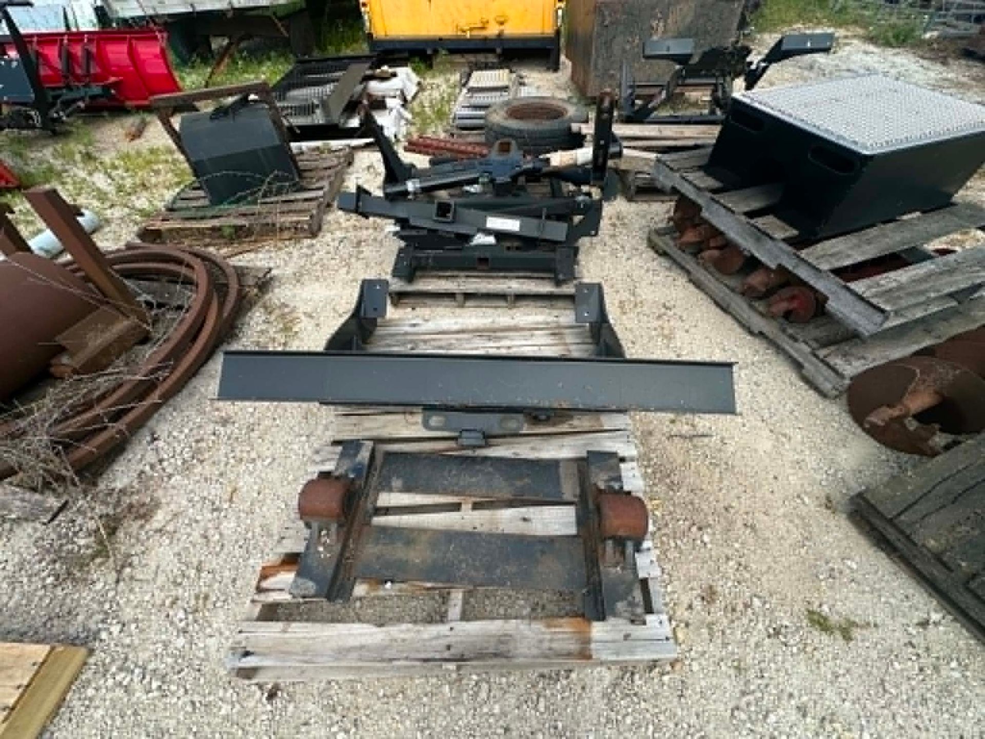 Old metal machinery frames and parts stacked outdoors on gravel in a scrapyard
